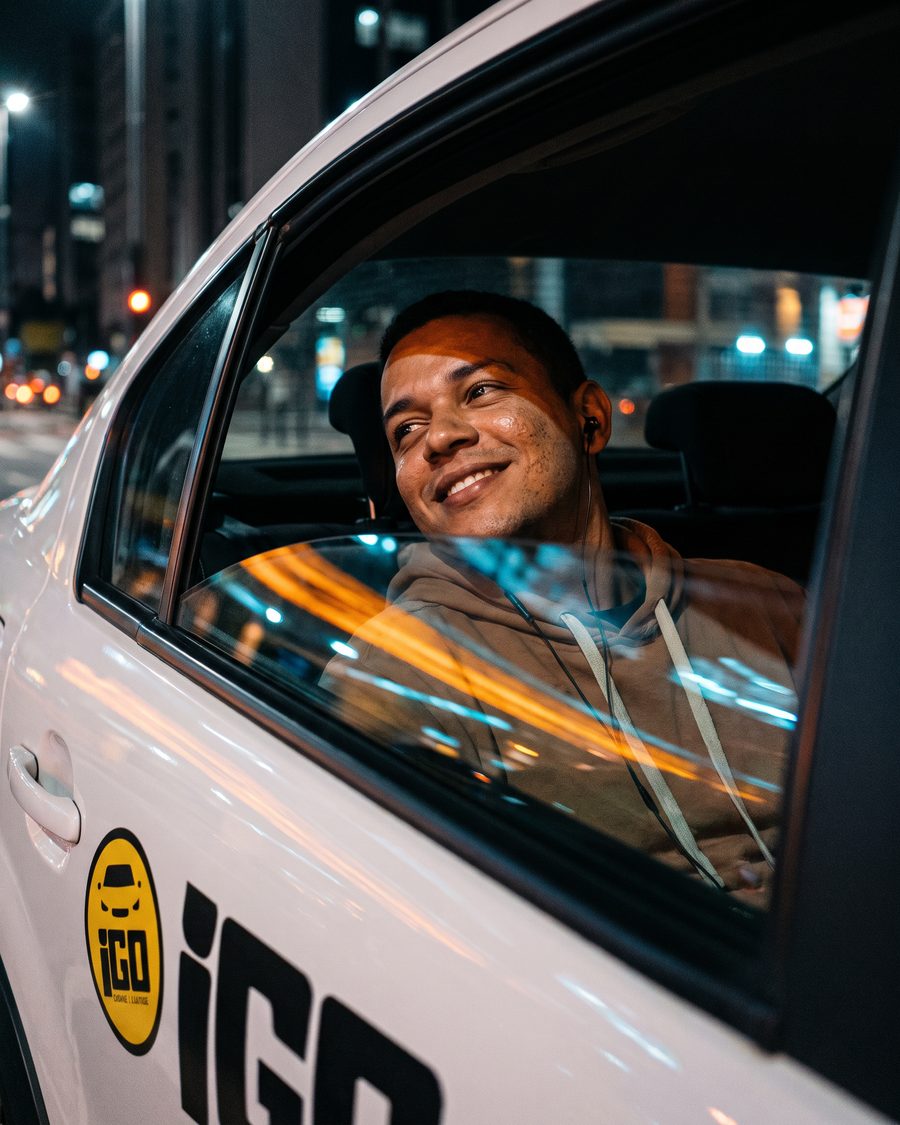 Passageiro no banco de trás de um carro da iGO Mobilidade à noite numa avenida de Marília